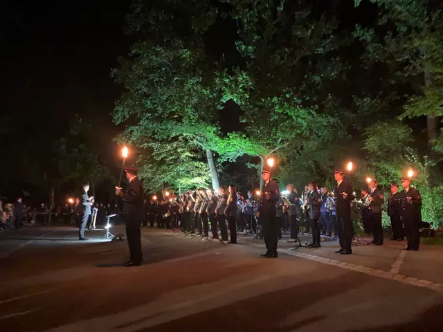 Musiker und Fackelträger stehen vor einer Baumreihe