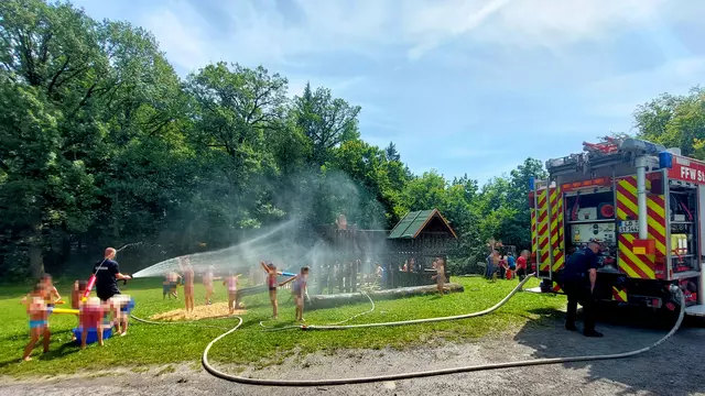 Feuerwehrleute spritzen mit Wasserschläuchen die Kinder nass