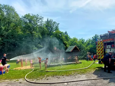 Feuerwehrleute spritzen mit Wasserschläuchen die Kinder nass